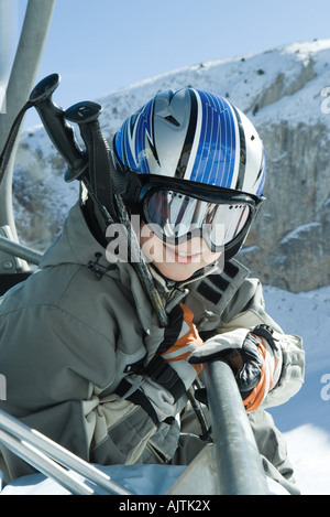 Junge Skifahrer im Sessellift, gekleidet in Skibrillen und Helm, lächelnd in die Kamera, Porträt Stockfoto