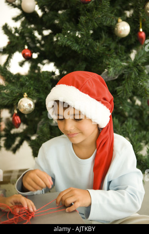 Junge öffnen vor Weihnachtsbaum, Santa tragen Hut, Lächeln Stockfoto