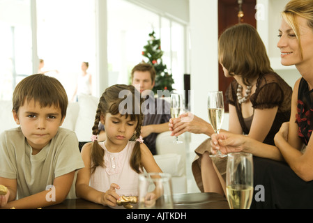 Zwei Kinder halten Weihnachtsschmuck, Erwachsene Champagner trinken Stockfoto