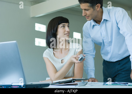 Junge Geschäftsfrau sitzen am Schreibtisch, Handy, halten, sich mit einem Blick auf männlicher Kollege Stockfoto