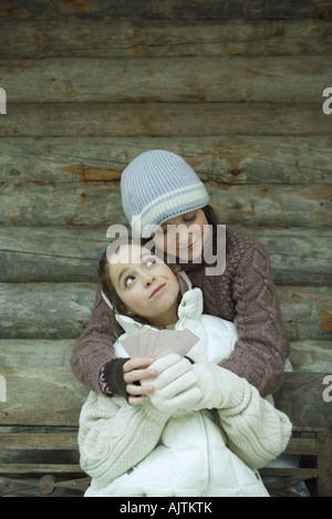 Junge Freunde in Winterkleidung, gibt man mit Karten, während die andere ihr eine Umarmung Stockfoto