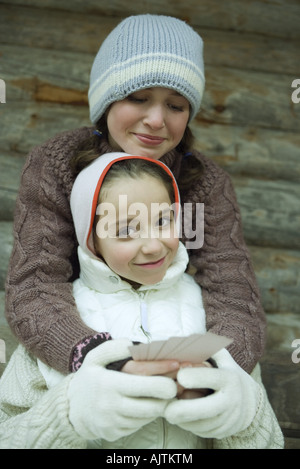 Junge Freunde in Winterkleidung, gibt man mit Karten, während die andere ihr eine Umarmung Stockfoto