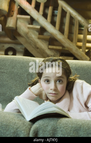Preteen Mädchen auf dem Sofa liegend mit Buch, Blick in die Kamera Stockfoto