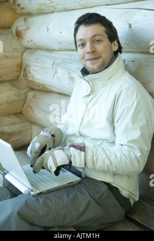 Mann mit Laptop mit Handschuhen, lächelnd in die Kamera Stockfoto