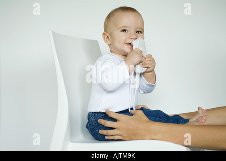 Baby-Sitter in Stuhl setzen Schuh in Mund, die arme Mutter halten Babys Beine Stockfoto