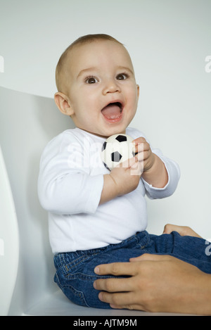 Baby-Sitter im Stuhl halten Ball, Mutters Hände halten Babys Beine Stockfoto