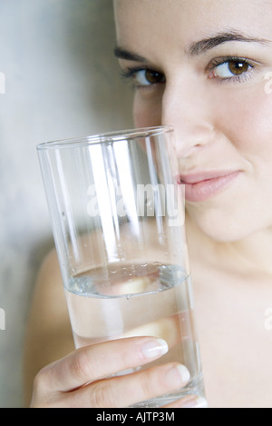 Junge Frau mit Glas Wasser, lächelnd in die Kamera, beschnitten Ansicht Stockfoto