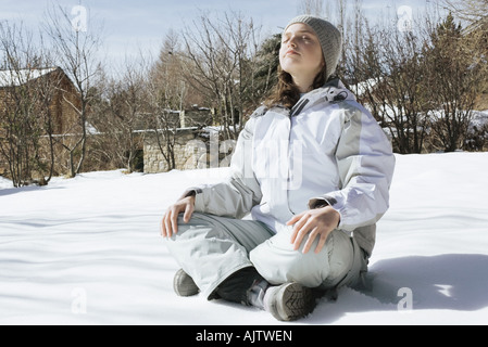 Teenager-Mädchen indischen Stil auf Schnee sitzend, mit geschlossenen Augen und Kopf nach hinten, in voller Länge Stockfoto