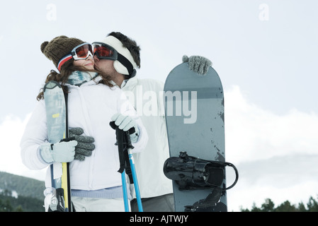 Junges Paar draußen mit Ski und Snowboard, Mann, Freundin Wange küssen Stockfoto