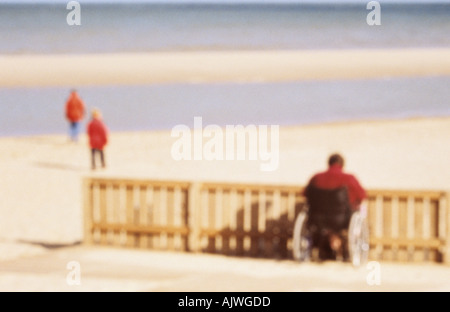 Defokussierten Person in einem Rollstuhl hielten wir an ein Hindernis auf dem Strand, Blick auf den See und zwei andere Figuren Stockfoto