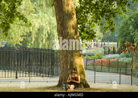 Horizontale Porträt einer attraktiven jungen Frau, die ihr Buch unter dem Schatten eines Baumes in der Sonne. Stockfoto