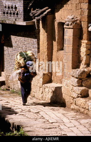 Asien, China, Provinz Yunnan Lijiang. Naxi Frau trägt Korb von Produkten in der Altstadt Stockfoto