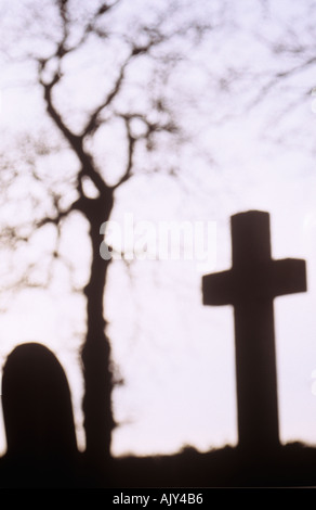 Grabsteine auf einem Friedhof mit Weißdorn oder Mai oder Crataegus Monogyna Baum Silhouette gegen ein Winterhimmel Stockfoto