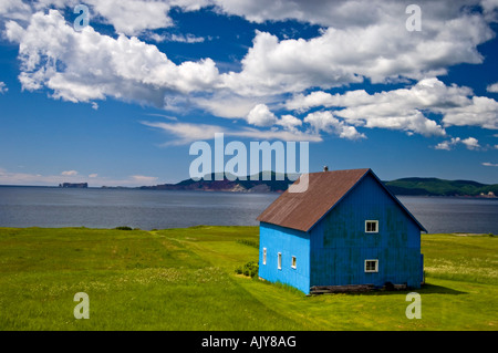 Blaue Scheune mit Blick auf Baie de Malbaieand distant Rocher Percé (Rock), Gaspé (Belle Anse), QC Quebec, Kanada Stockfoto