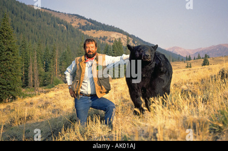 Ein Mann steht neben einem Schwarzbären in einer hohen Wiese im Norden von New Mexico Stockfoto