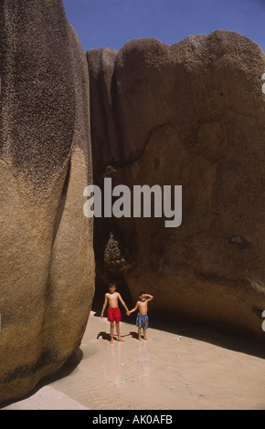 Zwei Jungen stehen zwischen massiven Granitfelsen am Strand Anse Source d'Argent auf der Insel La Digue auf den Seychellen. Stockfoto