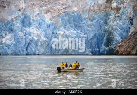 Ein kleines Boot, gefüllt mit Besuchern aus einem größeren Kreuzfahrtschiff navigiert den Eisberg-Fluss unter einem gewaltigen Gletscher Stockfoto