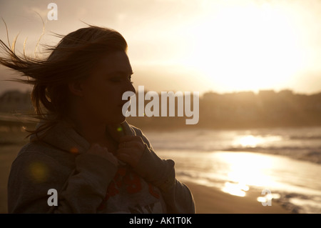 Studentin steht auf einem Strand bei Sonnenuntergang Blick auf das Meer mit den Augen geschlossen mit Haaren im wind Stockfoto