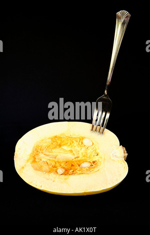 Halb eine gelbe farbige Spaghetti-Kürbis mit Samen und Fruchtfleisch im Zentrum und Gabel stecken senkrecht im rechten oberen Bereich. Stockfoto