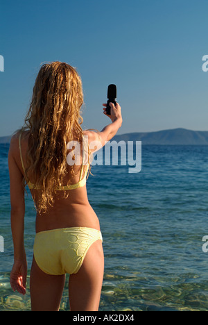 Junge Frau, die eine Aufnahme mit einer Handy-Kamera stehen am Strand Stockfoto