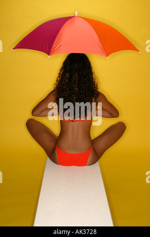 Frau in orange Bikini mit Regenschirm auf Sprungbrett Stockfoto