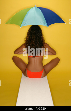 Frau in orange Bikini mit Regenschirm auf Sprungbrett Stockfoto