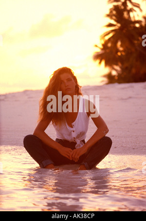 Malediven. Junge Frau sitzen am tropischen Strand bei Sonnenuntergang Beinen. Stockfoto