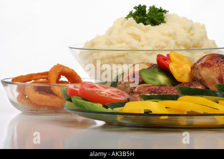 Gebratenes Hähnchenfleisch auf einem Glasteller mit Kartoffelpüree in der Schüssel gebratene Zwiebelringe Lebensmittelüberzug künstlerische Nahaufnahme niemand typisch USA Hi-res Stockfoto