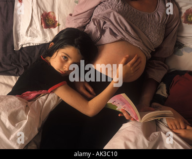 Ein junges Mädchen hören ihre schwangere Mutter, eine Geschichte zu lesen, um sie und ihren Bruder im Bett, UK. Stockfoto