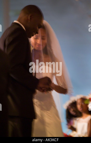 Eine Mischrasse Braut blickt auf afroamerikanische Bräutigam setzen den Ring an ihrem Finger während ihrer Hochzeit in Santa Ana, Kalifornien Stockfoto