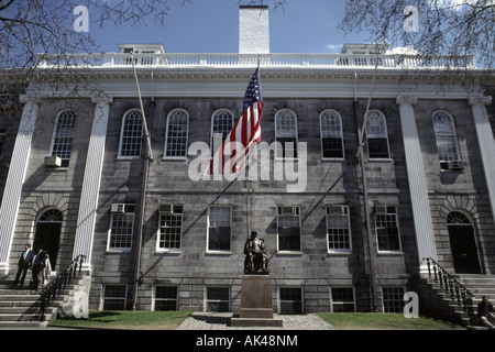 Eine Statue von John Harvard sitzt unter einer großen Amerika-Flagge auf dem Campus der Harvard University in Cambridge, Massachusetts Stockfoto