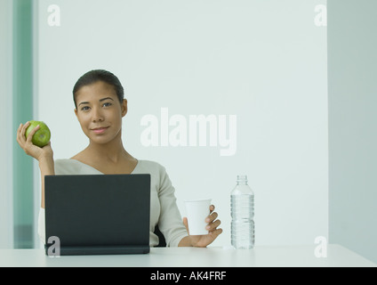 Frau sitzt am Laptop, mit Glas Wasser und Apfel Stockfoto