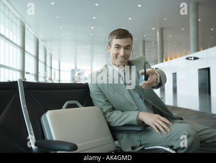 Geschäftsmann, sitzen im Flughafen-Lounge, durchhalten Handy in Richtung Kamera Stockfoto