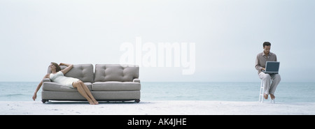 Am Strand sitzt Frau Nickerchen auf der Couch während Mann auf Stuhl mit computer Stockfoto