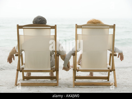 Paar, sitzen in Liegestühlen, Hand in Hand, Rückansicht Stockfoto