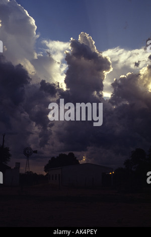 Schulmühle und Bäume gegen den Himmel mit großen stürmischen Wolken und Lichtstrahlen. Am späten Nachmittag. Formosa, Argentinien Stockfoto