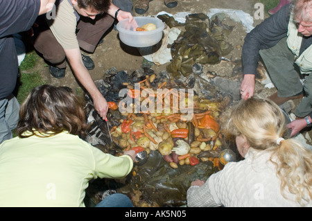 Eröffnung der Grube Ofen bei einem Curanto heißen Kochen in einer Grube Ofen Gemüse und Fleisch kochen auf Steinen Stockfoto