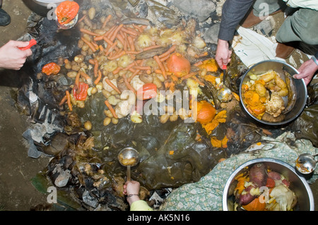 Eröffnung der Grube Ofen bei einem Curanto heißen Kochen in einer Grube Ofen Gemüse und Fleisch kochen auf Steinen Stockfoto