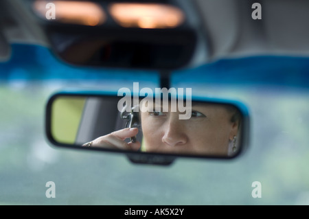 junge Autofahrerin mit Handy Kopfhörer reflektiert im Spiegel der hinteren Ansicht Stockfoto