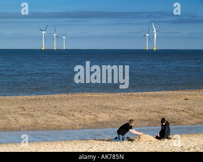 Jungs machen eine Sandburg am Strand mit fünf Turbinen der Scroby Sands Offshore-Windpark hinter. Stockfoto