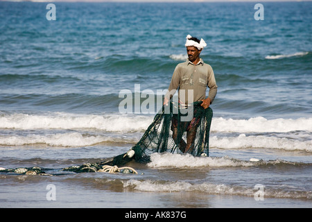 Omanischer Fischer am Strand im Nahen Osten, der im Meer im Netz steht und seine Netze im Oman überprüft Stockfoto