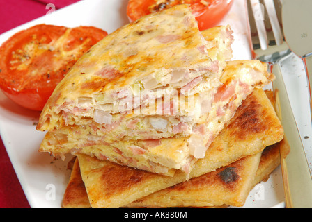 Frühstück mit Käse und Speck-Omelett-Scheiben auf irischen Farls (Kartoffelbrot) mit gegrillten Tomaten. Stockfoto