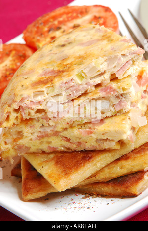Frühstück mit Käse und Speck-Omelett-Scheiben auf irischen Farls (Kartoffelbrot) mit gegrillten Tomaten. Stockfoto