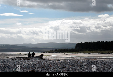 TOURISTEN MACHEN SIE EINE PAUSE AUF EINEM BAUMSTAMM IN FINDHORN BAY AUF DER NORDÖSTLICHEN SCHOTTISCHEN KÜSTE IN DER NÄHE VON INVERNESS.UK Stockfoto