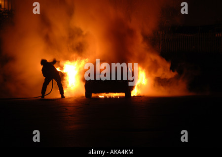 Einzelne Feuerwehrmann Kämpfe allein zu Auto Feuer die Hitze ausweichen und gleichzeitig Ziel seiner Wasserschlauch Stockfoto