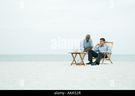 Zwei Männer am Strand, Blick auf Laptop-Computer zusammen, volle Länge Stockfoto