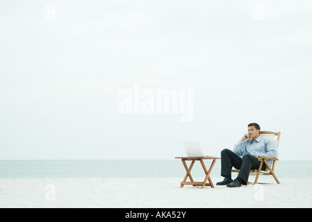 Man sitzt im Stuhl am Strand, Blick auf Laptop-Computer, hand unter Kinn Stockfoto