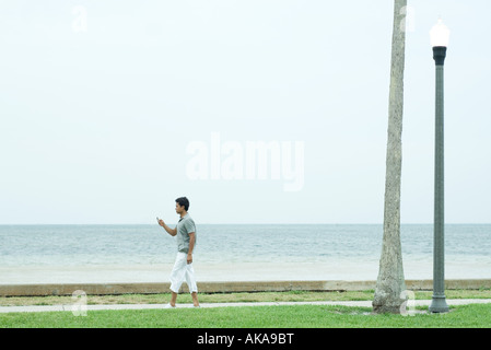 Mann zu Fuß auf Bürgersteig am Strand, Blick auf Handy Stockfoto