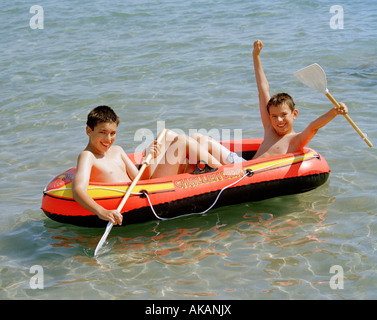 Zwei Jungen spielen in ein aufblasbares Boot im Meer. Stockfoto