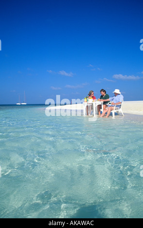 Gruppe von drei Personen im Wasser am Tisch sitzen am Rand des Meeres in den Malediven Indischer Ozean Stockfoto